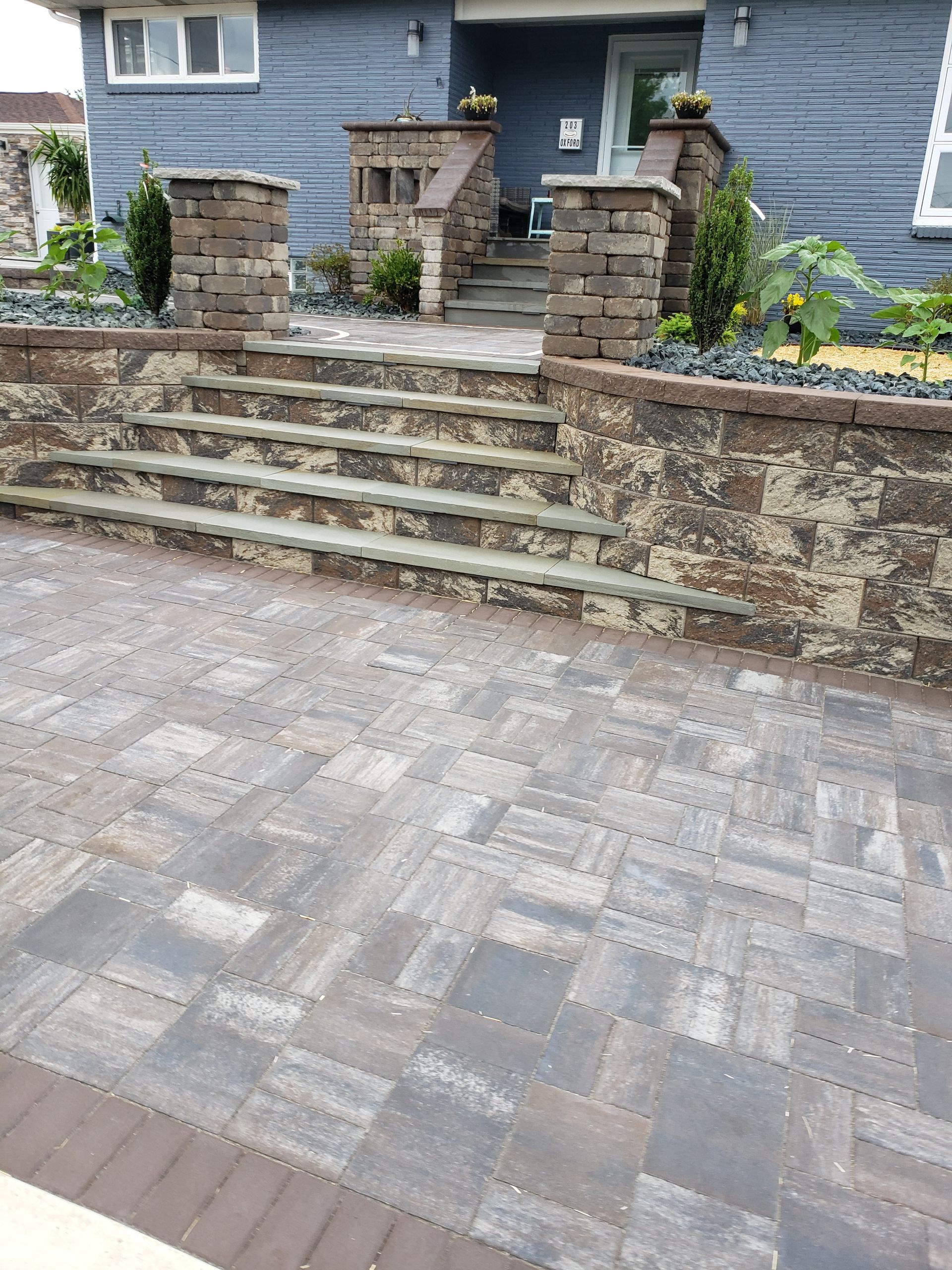 Stone steps with brick pillars lead up to a blue house front entrance, fronted by a stone paver patio.