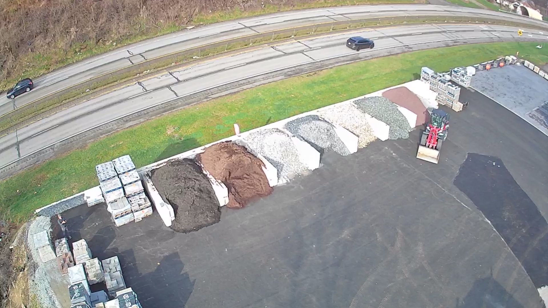 Aerial view of a landscape supply yard with piles of mulch and stone, organized in bins next to a paved road.
