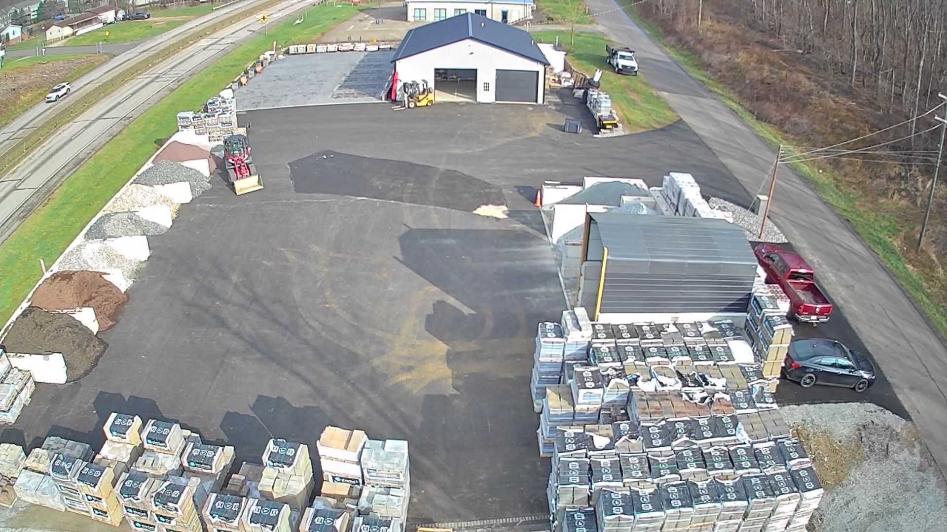 An aerial view of a landscape supply yard with gravel, mulch piles, palletized materials, and a warehouse building.