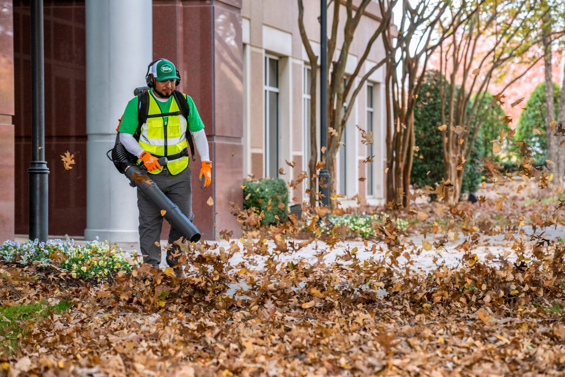 Person blowing leaves with a leaf blower near a building.