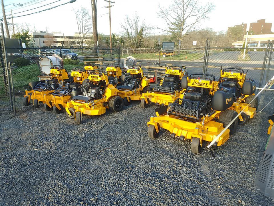 A row of yellow lawn mowers are parked in a gravel lot.