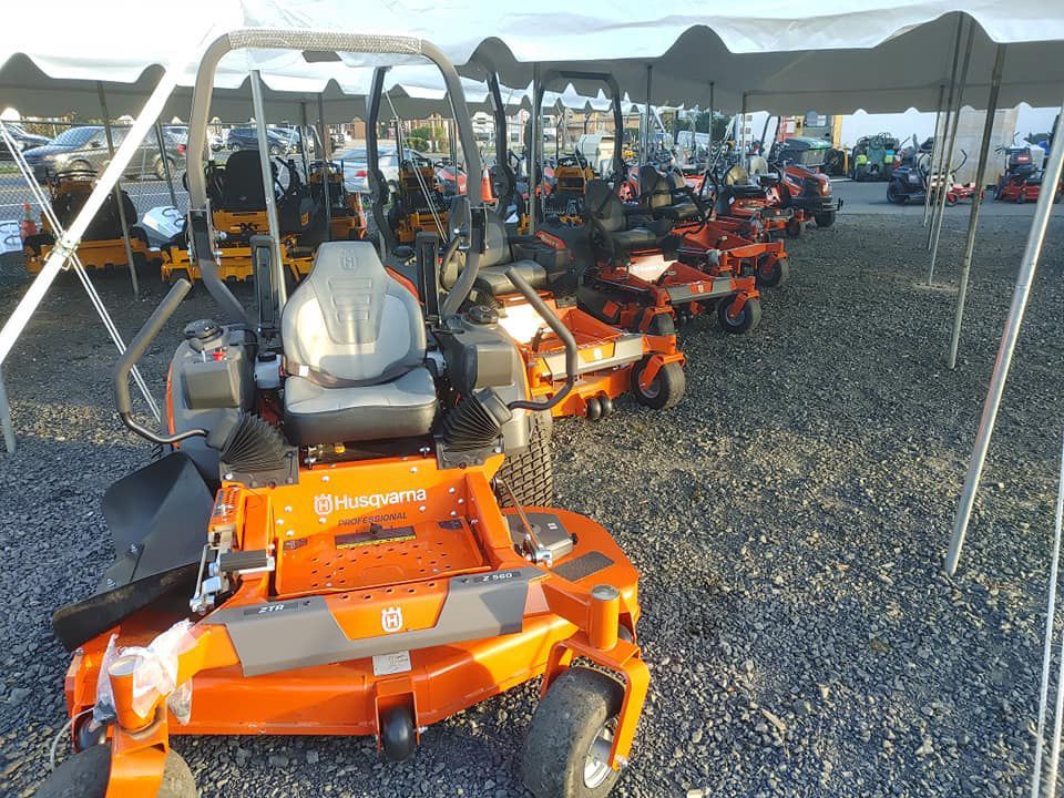 A row of lawn mowers are parked under a tent.