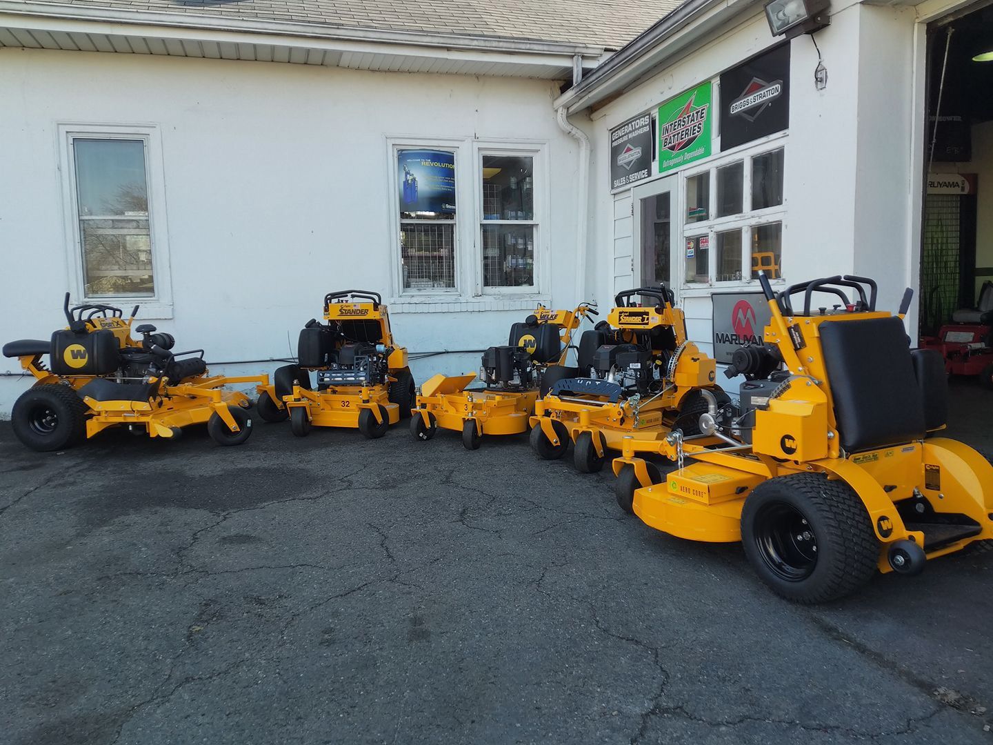 Three yellow lawn mowers are parked in front of a building
