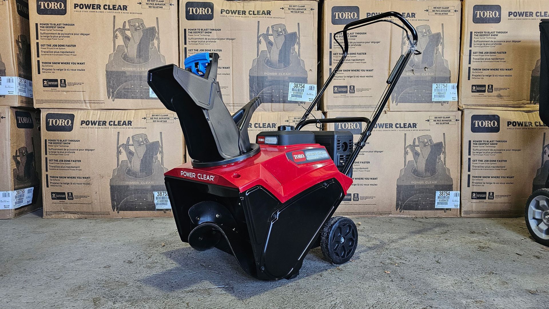 A red snow blower is sitting in front of a stack of boxes.