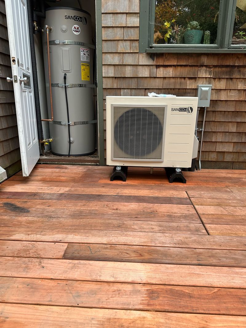 A heat pump is sitting on a wooden deck next to a water heater.