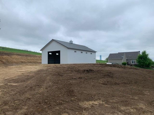 a white barn is sitting on top of a dirt hill next to a house