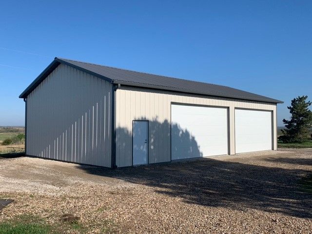 a large metal building with two garage doors is sitting on top of a gravel road