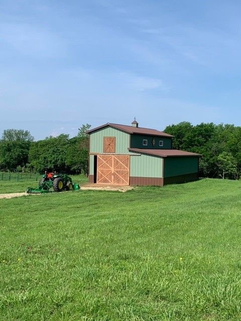 a tractor is parked in front of a barn in a grassy field