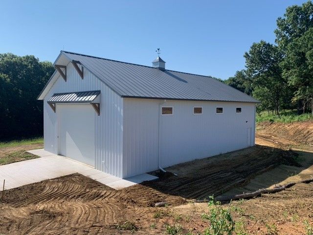 a white barn is sitting in the middle of a dirt field