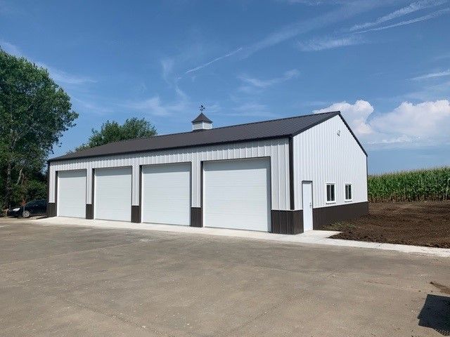 a white and brown garage with four garage doors is sitting on top of a dirt field