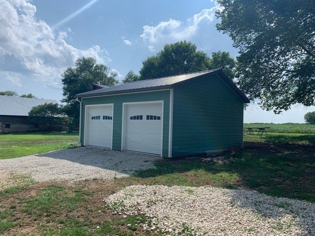 a green garage with two white garage doors is sitting in the middle of a grassy field