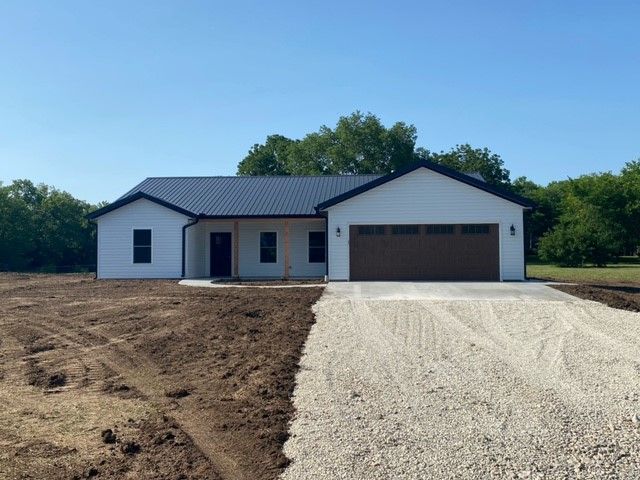 a white house with a brown garage door is sitting on top of a dirt field