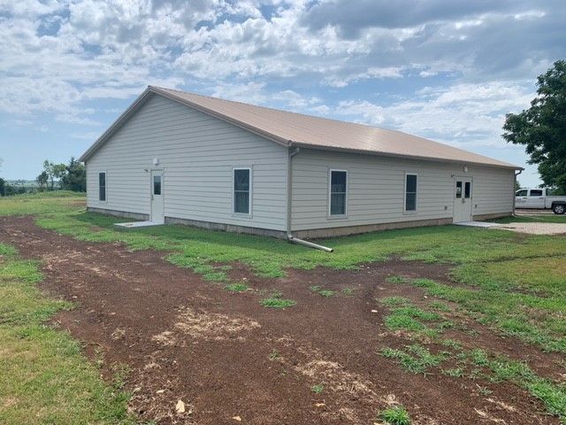 a large white house with a brown roof is sitting in the middle of a grassy field