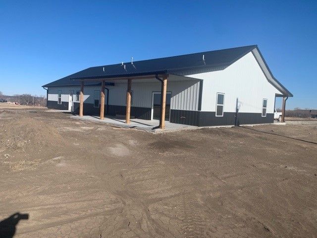 a large white house with a black roof is sitting in the middle of a dirt field