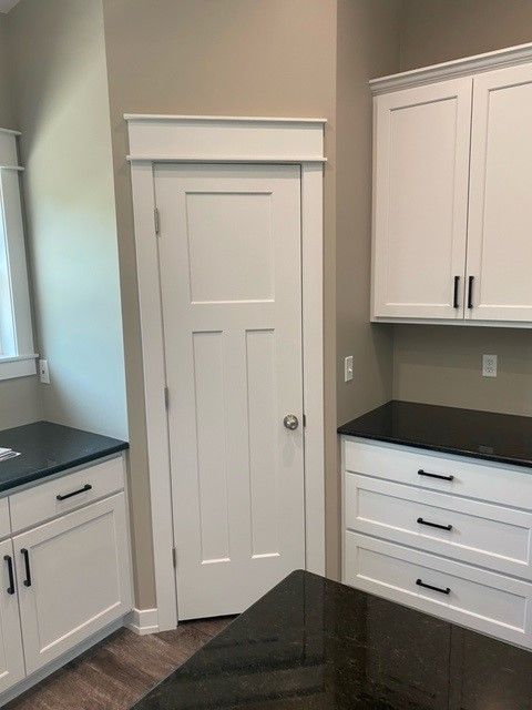 a kitchen with white cabinets, black counter tops, and a door