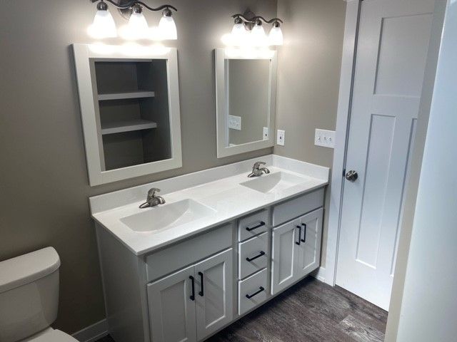 a bathroom with two sinks, two mirrors, and a toilet