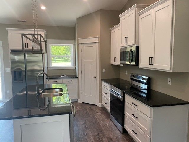 a kitchen with white cabinets, black countertops, stainless steel appliances, and a sink