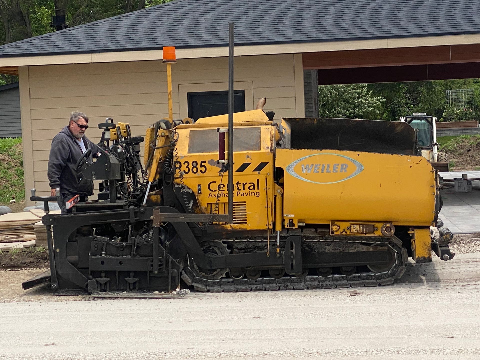 Yellow paving machine laying asphalt; worker nearby. Outdoors.