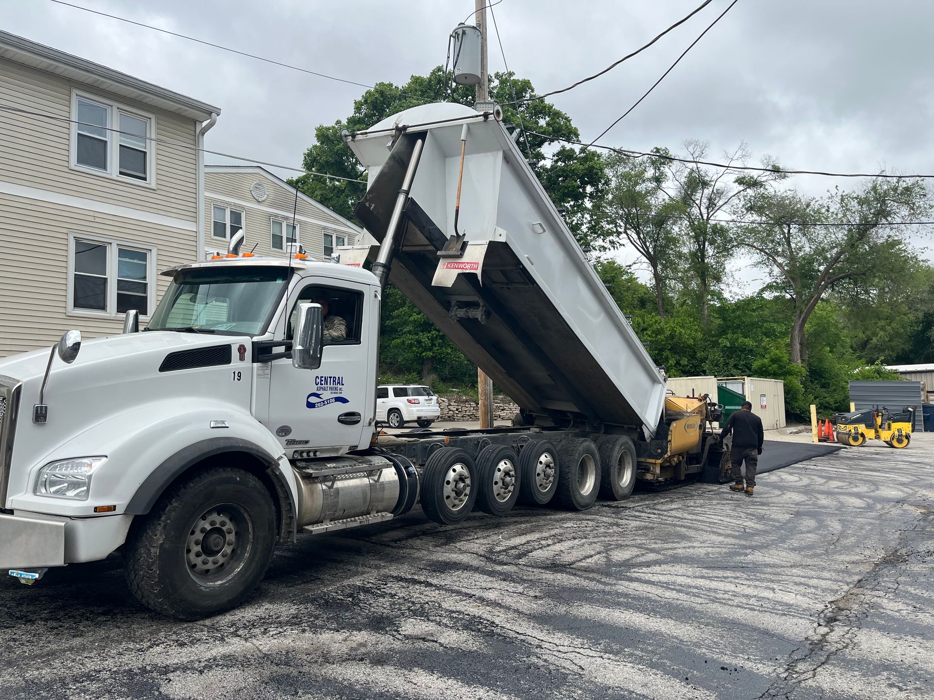 A dump truck is being loaded with asphalt in a parking lot.