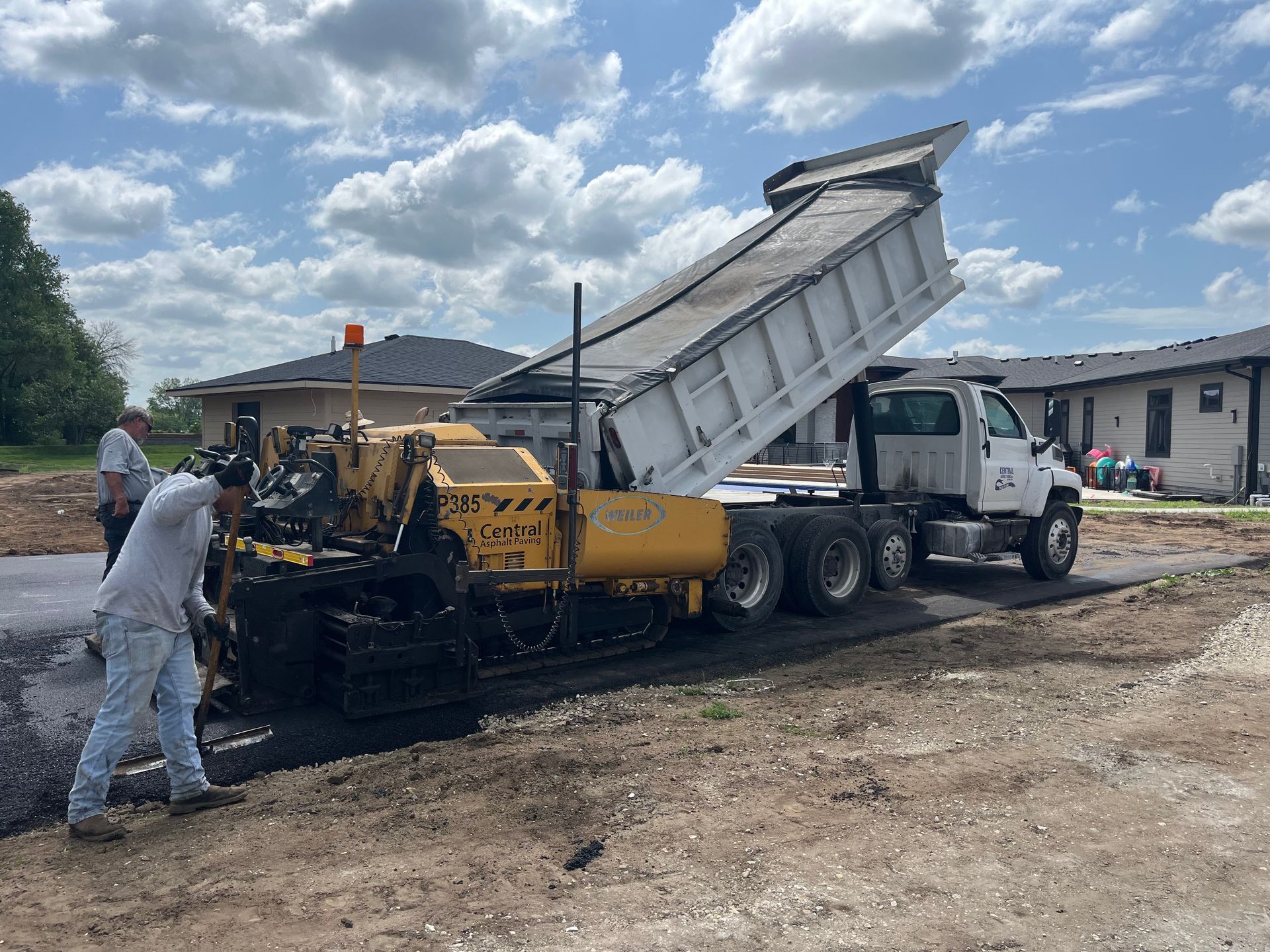 A dump truck is being loaded with asphalt on a construction site.
