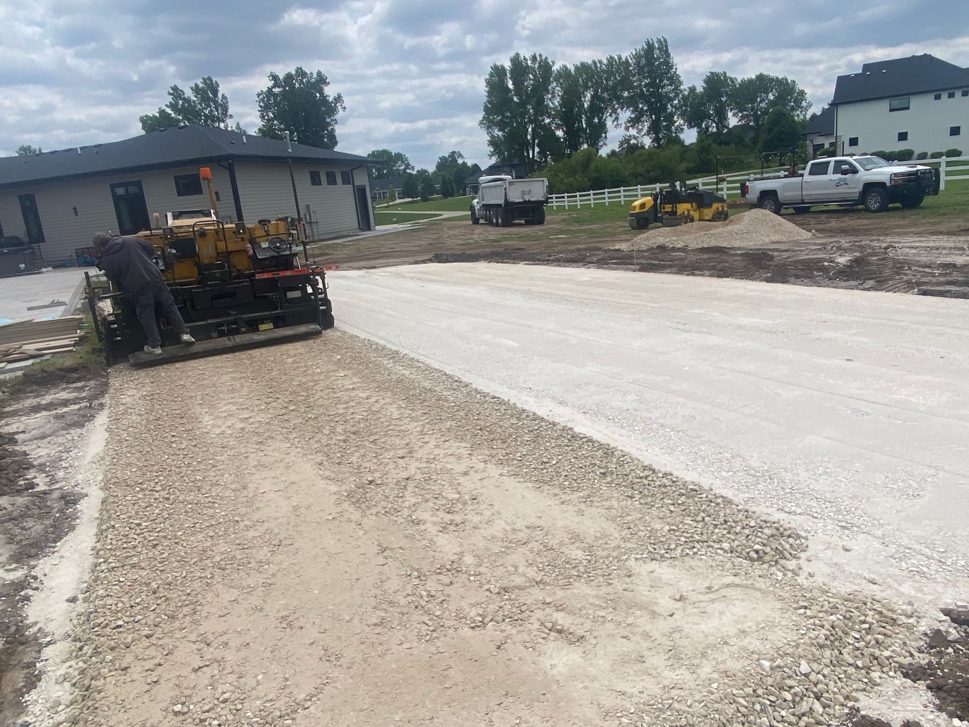 A construction worker operating paving machine laying gravel on a driveway.