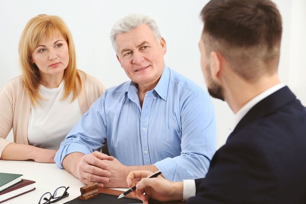 Three people in a meeting, talking across a table with documents and glasses.
