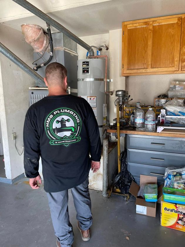 Person walking in a garage toward a water heater, with shelves, cabinets, and tools nearby.