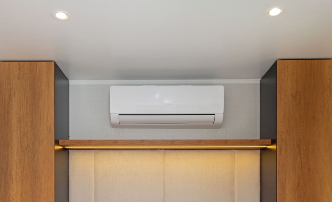 Wall-mounted white air conditioner above a wooden shelf in a modern room with recessed ceiling lights