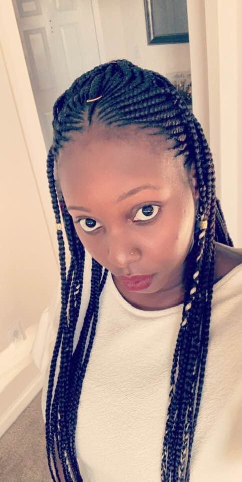 Woman with long braided hair wearing a white top, looking into the camera indoors.