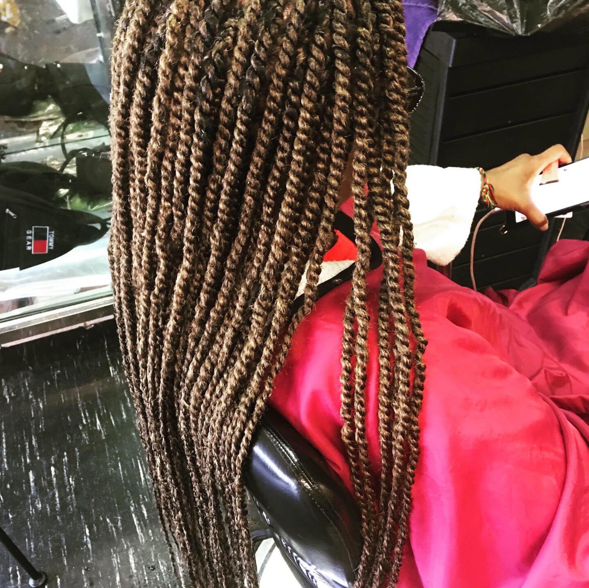 Back view of long brown braided hair with blonde highlights, seated in a car wearing a red wrap and white sleeve.