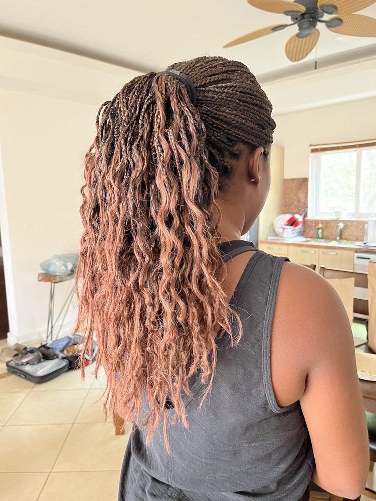 Back view of a person with long braids in a bright kitchen, wearing a dark tank top.