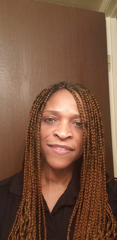 Woman with long braided hair smiling indoors against a brown door.