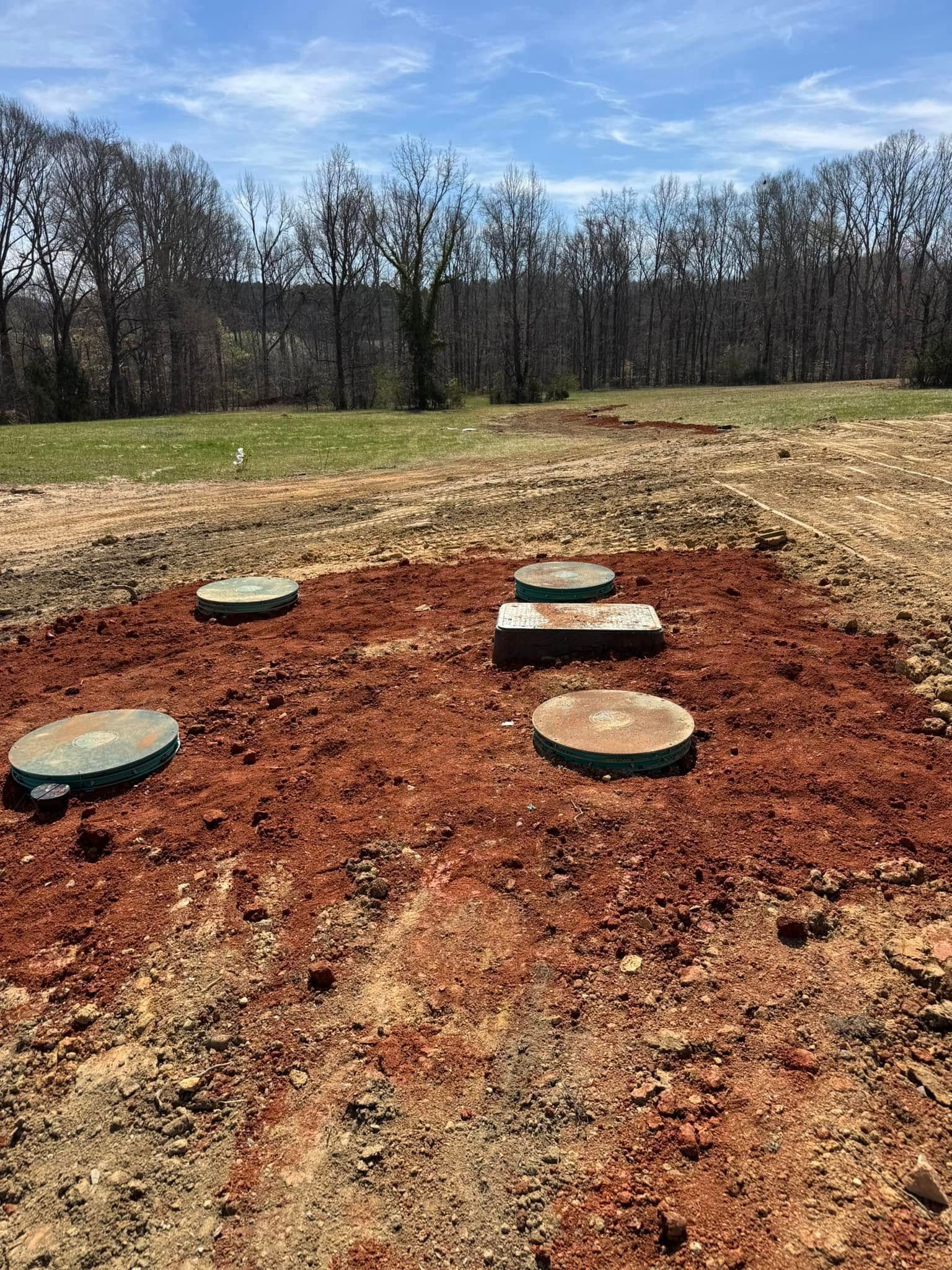 Five septic tank access lids on reddish-brown earth, under a partly cloudy sky.