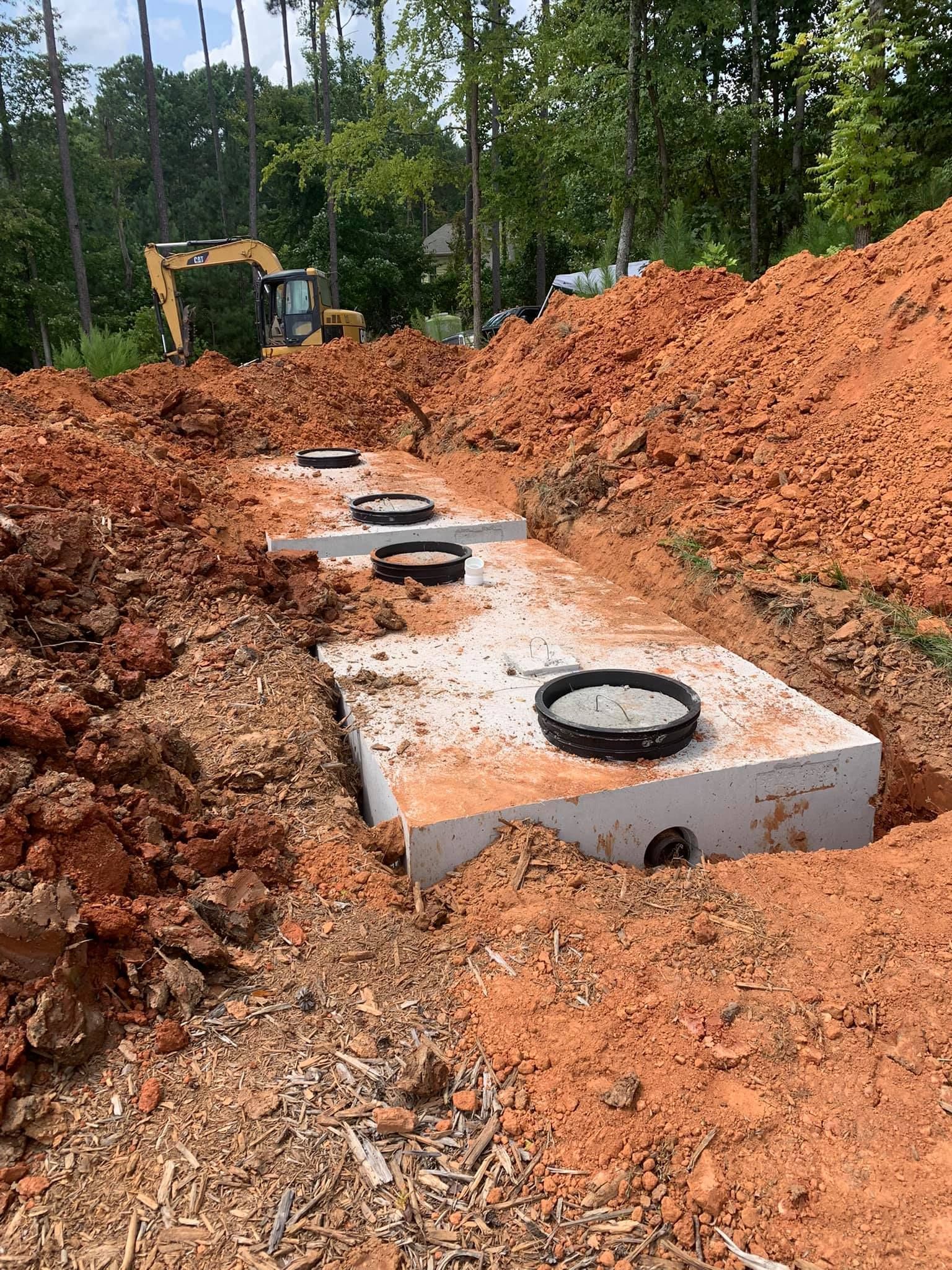 Concrete septic tank installation in a construction site with an excavator in the background.