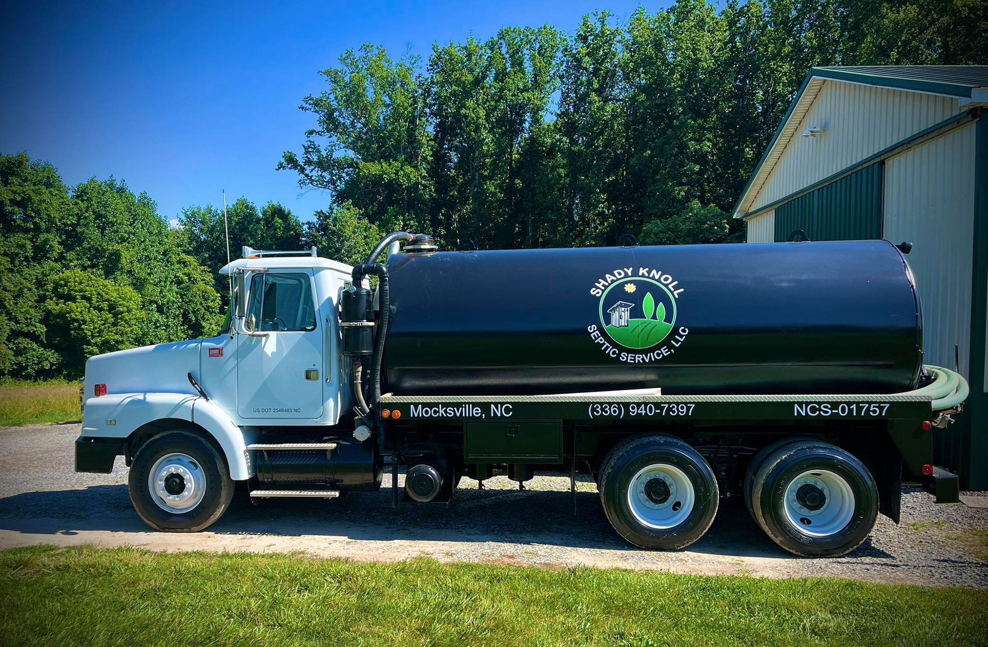 White septic service truck with black tank, green logo, parked outdoors on a sunny day.