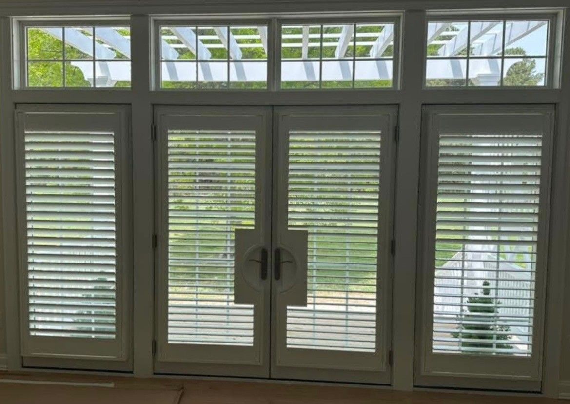 White French doors with shutters, topped by a trellis window, overlooking a green yard.