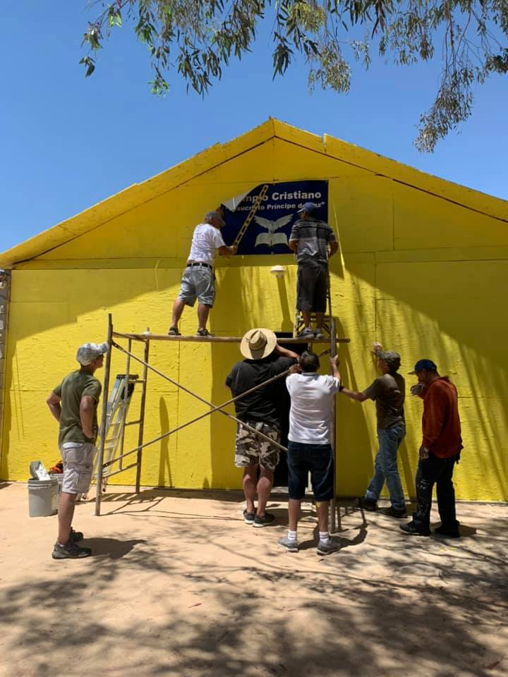 A group of people are painting a yellow building.