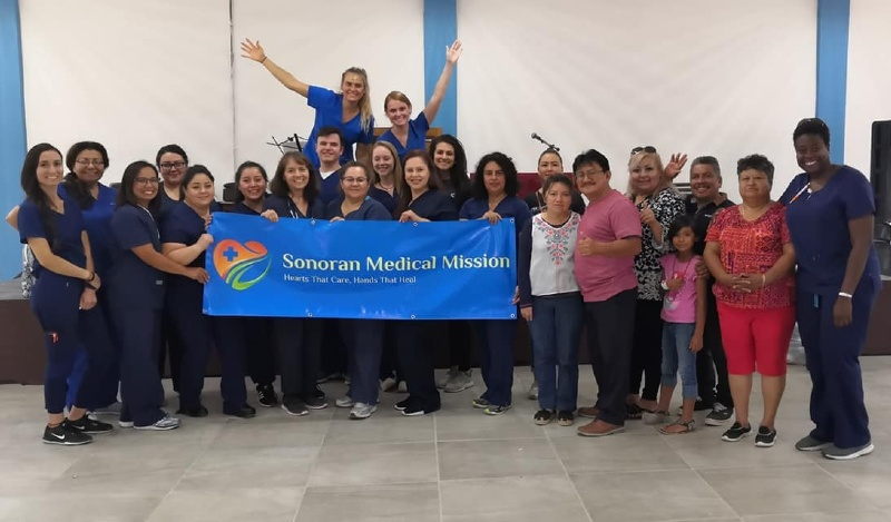 A group of people are posing for a picture while holding a blue banner that says service medical vision.
