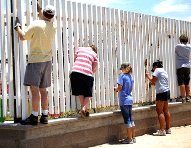 A group of people are painting a white fence