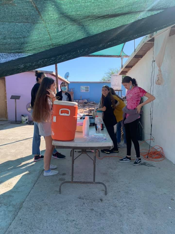 A group of people are standing around a table with an orange cooler on it.