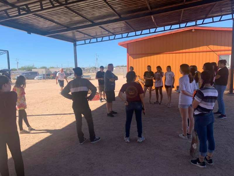 A group of people are standing in front of an orange building.