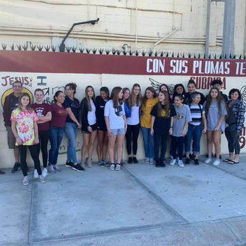 A group of people standing in front of a sign that says con sus plumas te