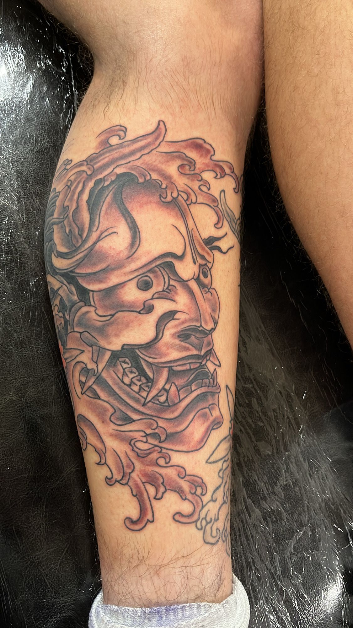 A person has a tattoo of a samurai mask on their leg.