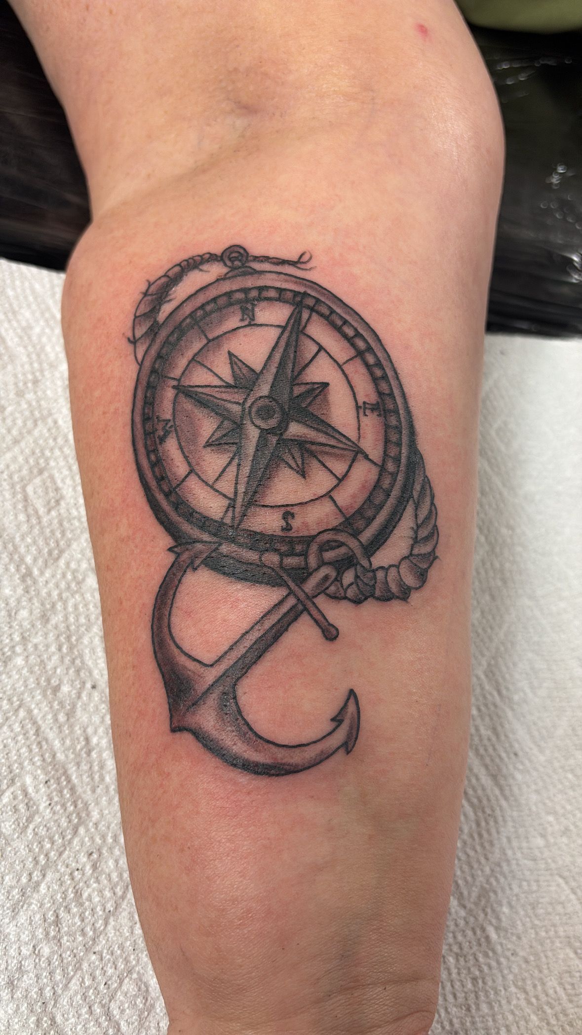 A person has a tattoo of a compass and anchor on their arm.
