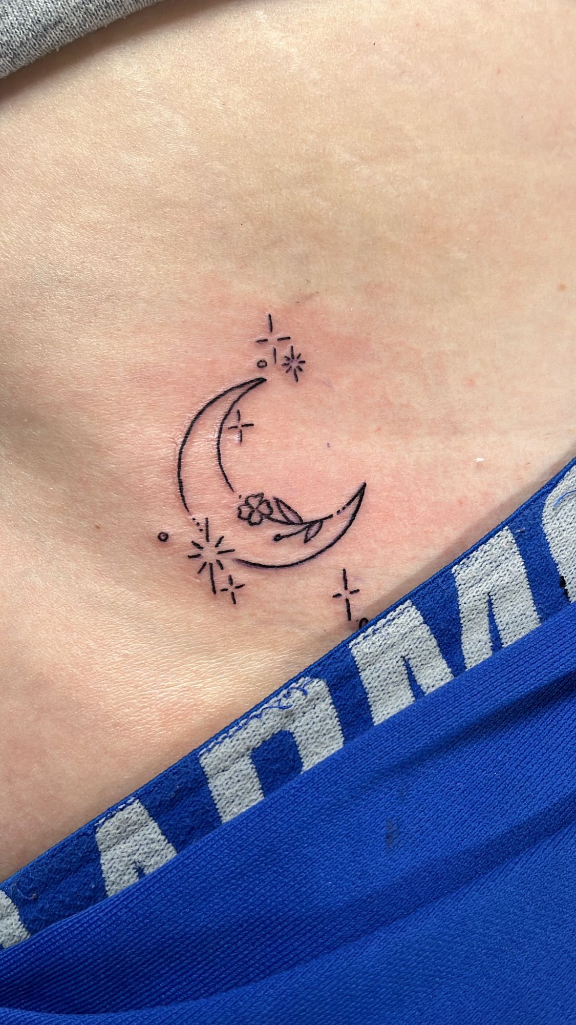 A small tattoo of a crescent moon and stars on a person 's stomach.