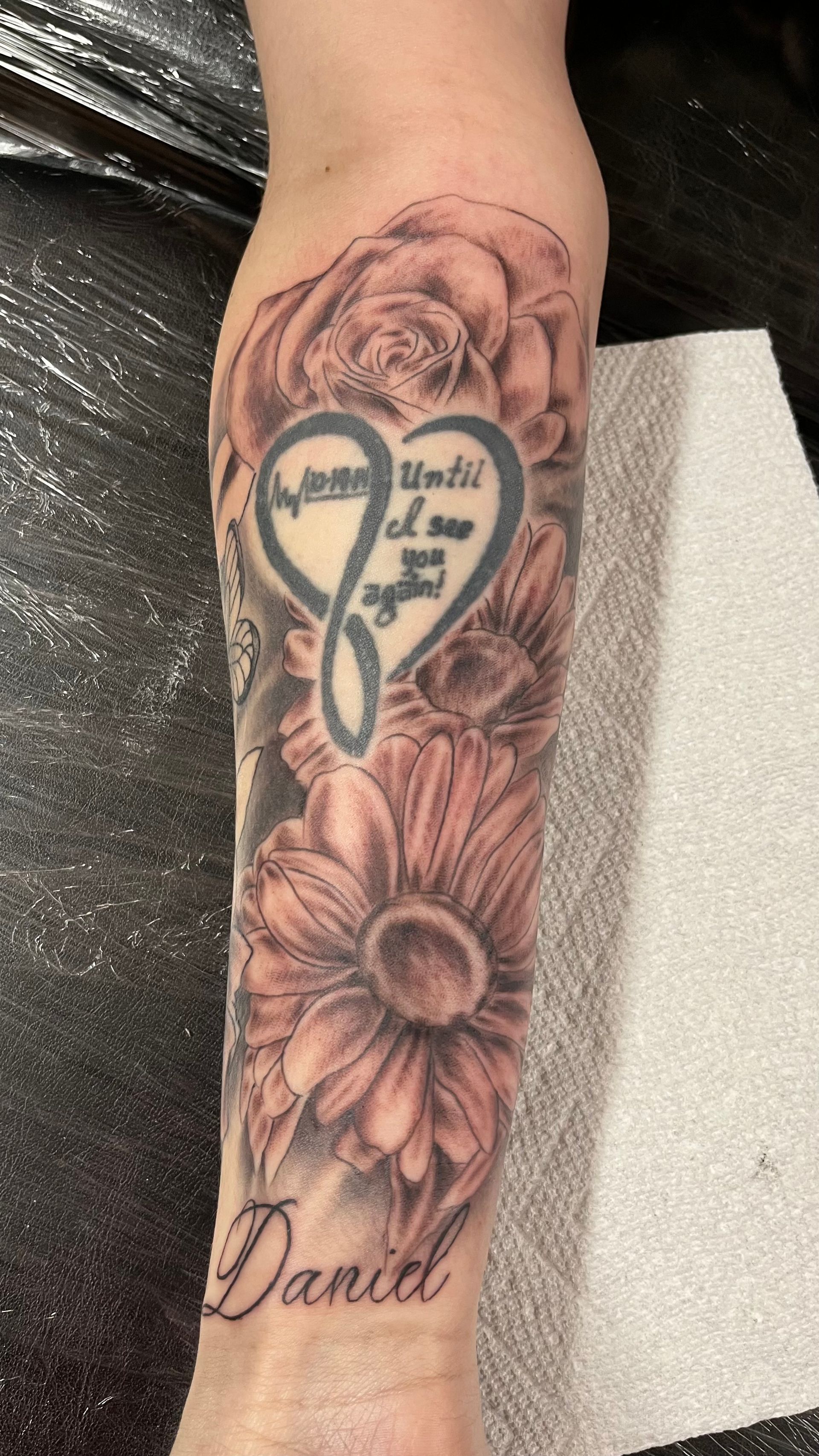 A person has a tattoo of a heart and flowers on their forearm.