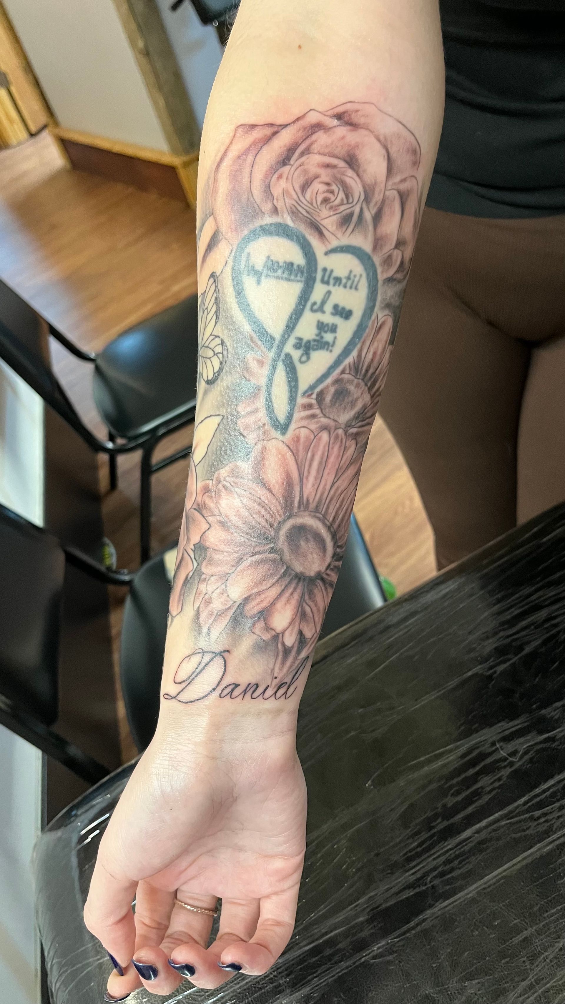 A woman has a tattoo of a heart and flowers on her forearm.