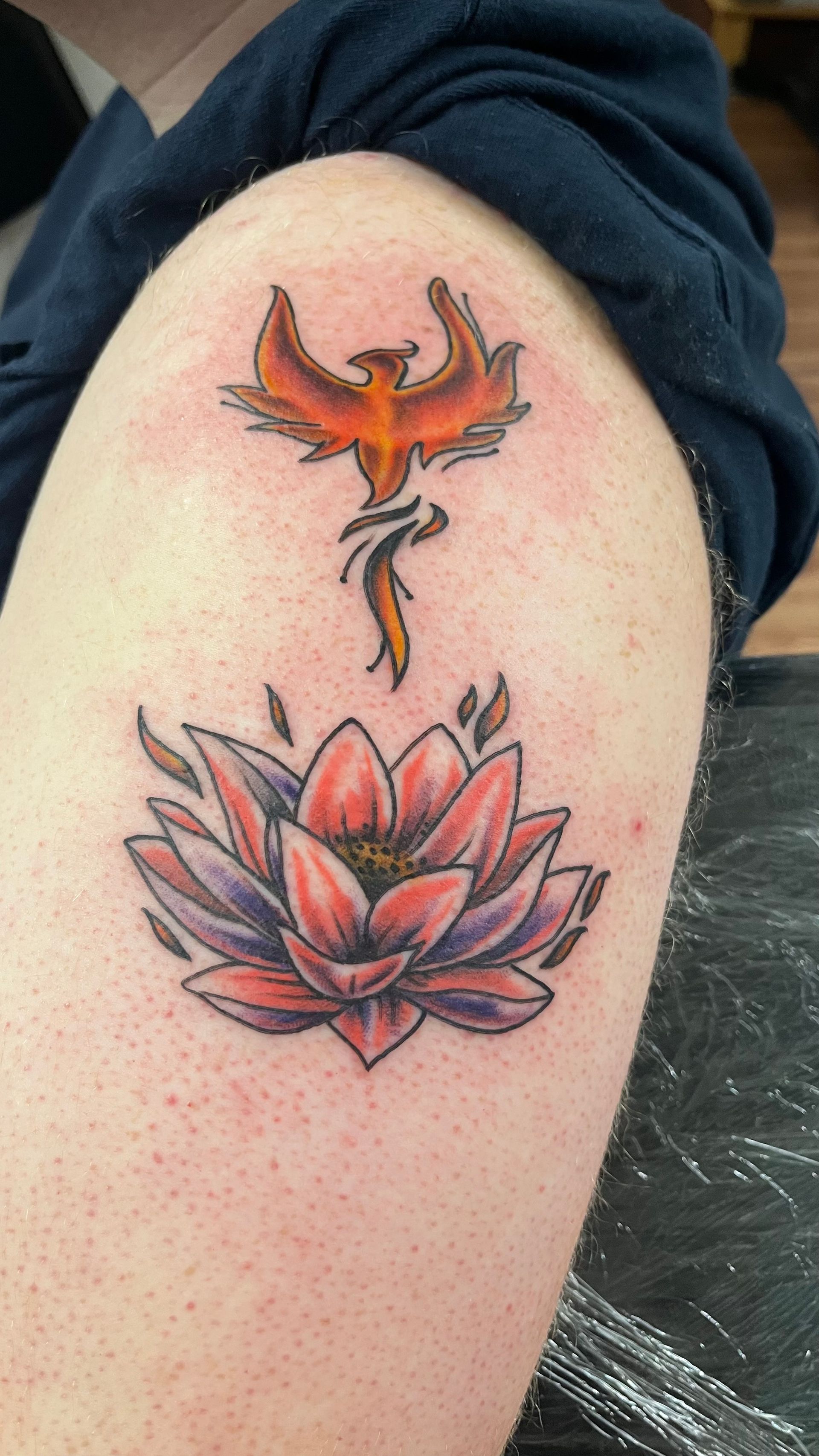 A person has a tattoo of a phoenix and a lotus flower on their arm.
