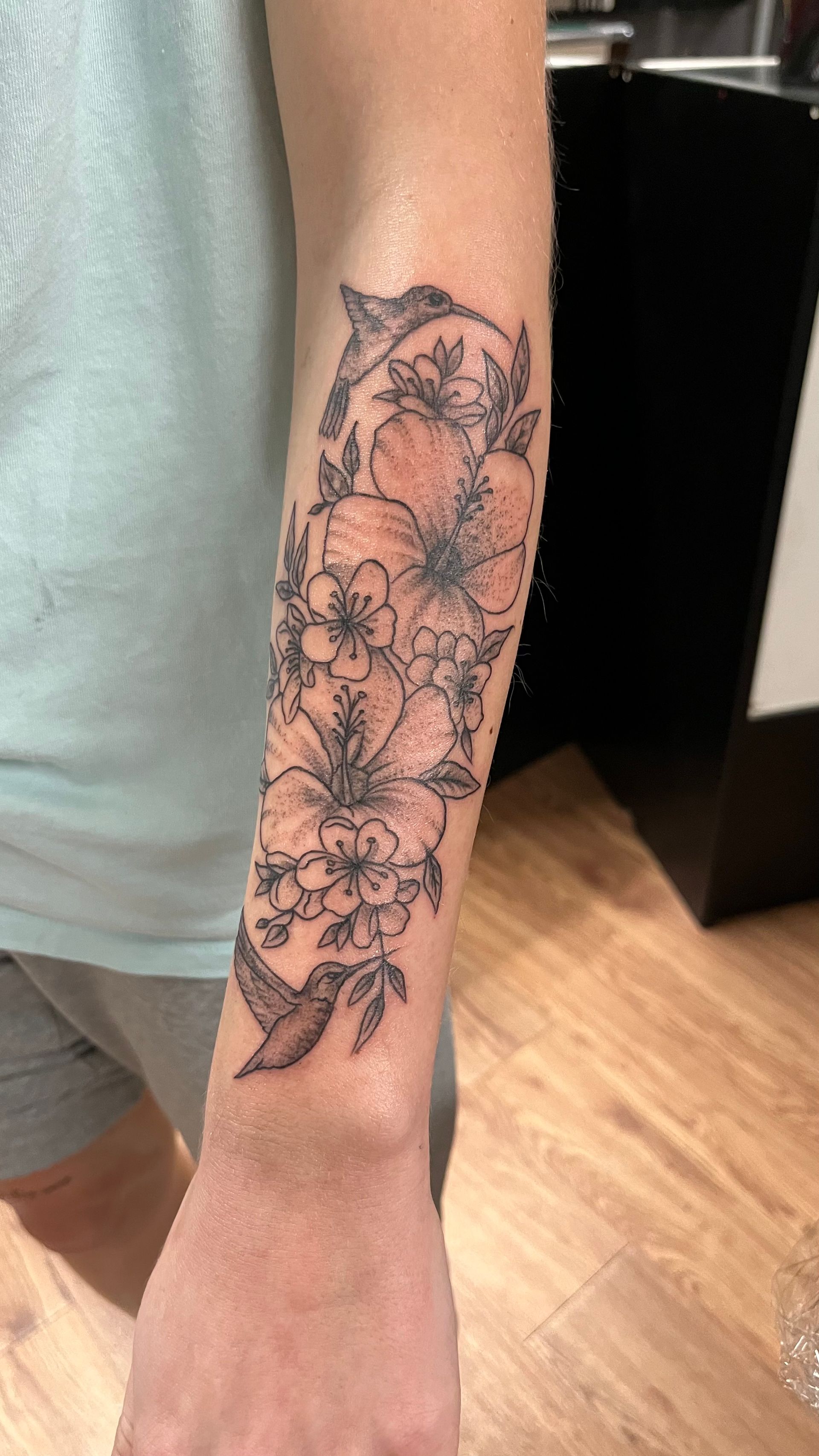 A person has a tattoo of flowers and a bird on their forearm.