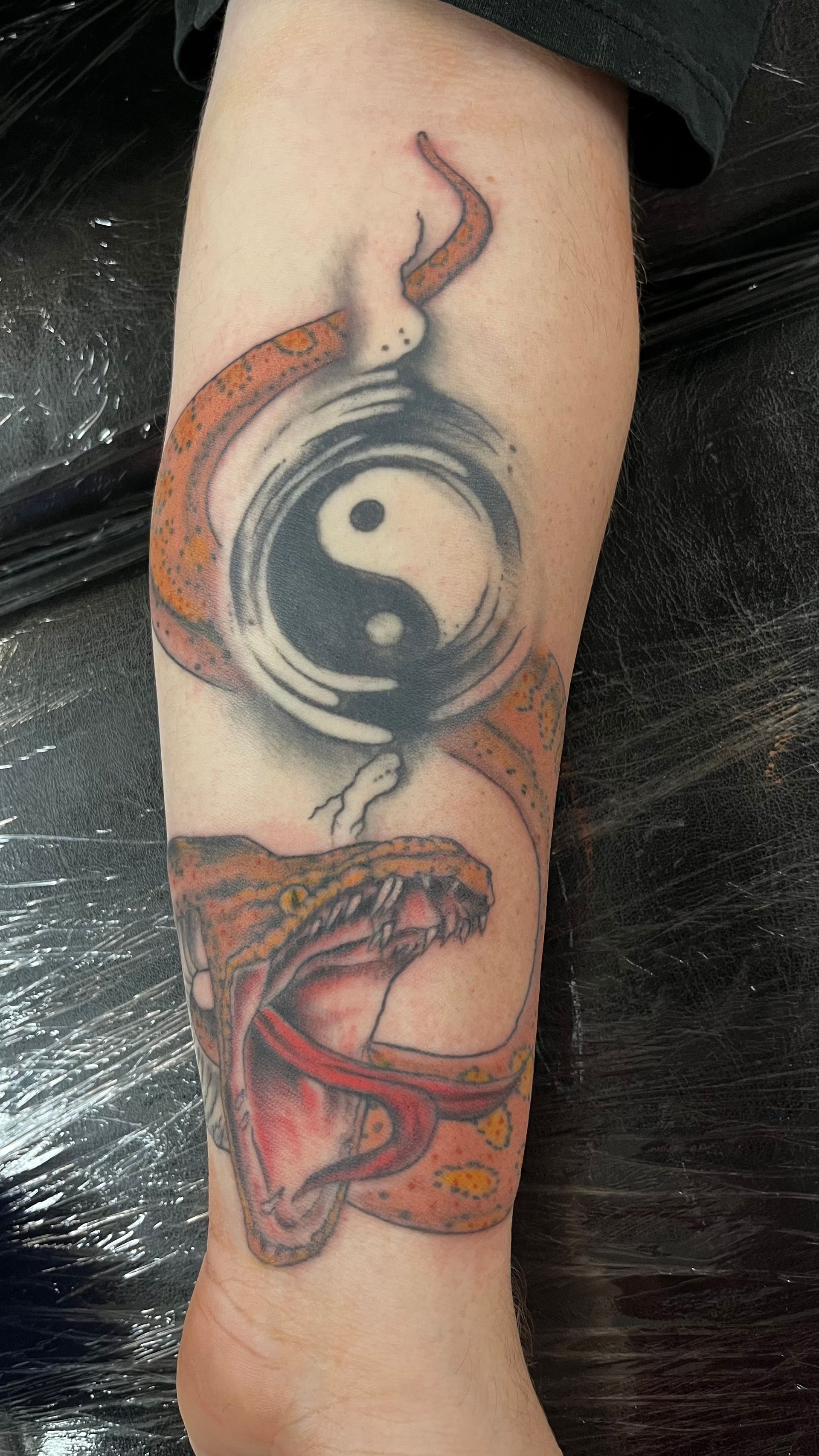 A person has a tattoo of a snake and a yin yang symbol on their leg.